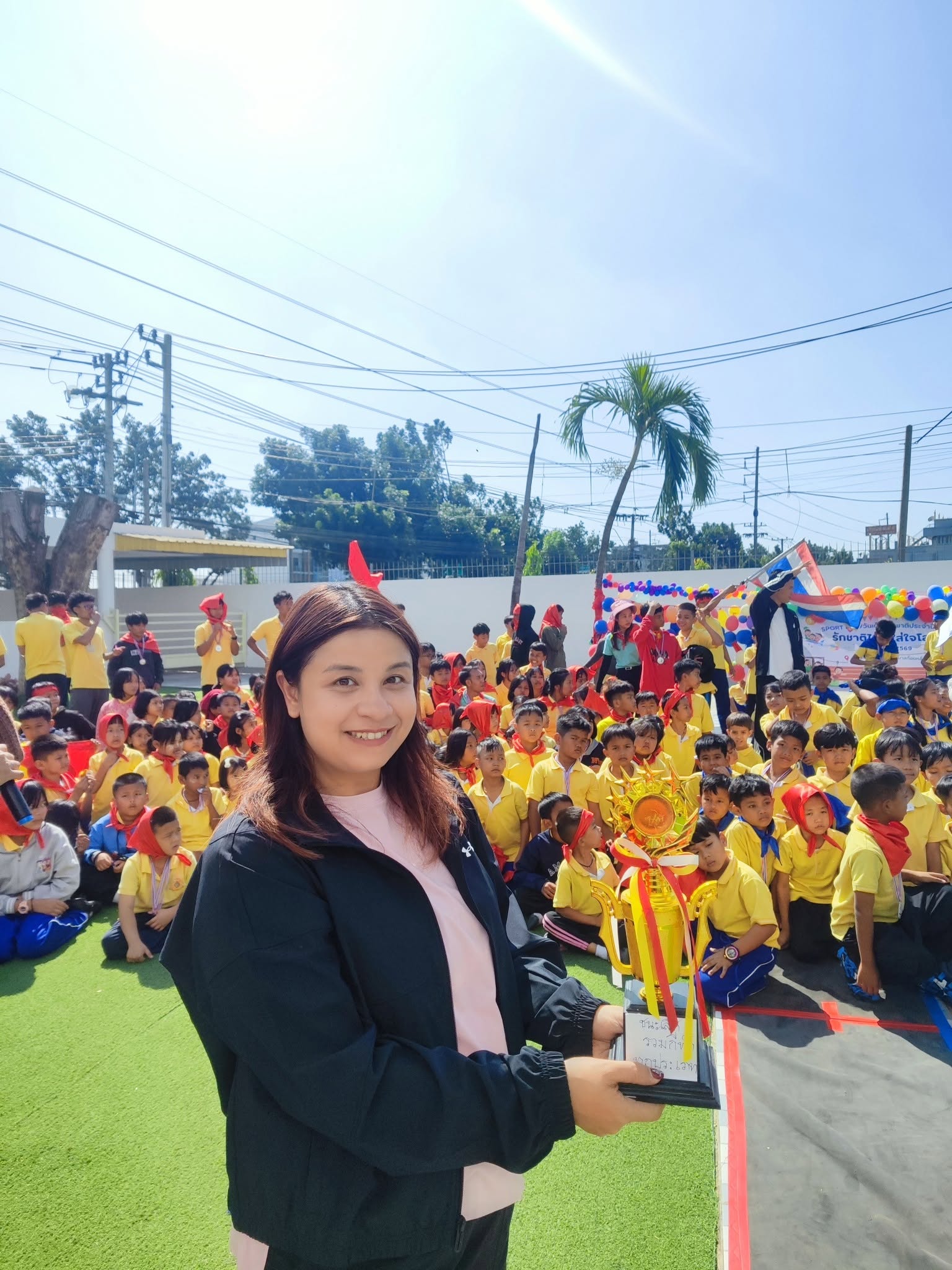 Kong Lah School teacher holding a trophy with students gathered behind her.